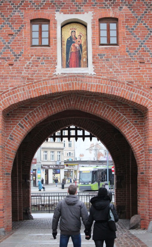 Durmazlar Panorama Olsztyn DRP5H05 #3020 na linii 1 skręcający z ulicy 11 Listopada na plac Jedności Słowiańskiej, widziany z ulicy Staromiejskiej przez przejście pod Wysoką Bramą (28 grudnia 2023)